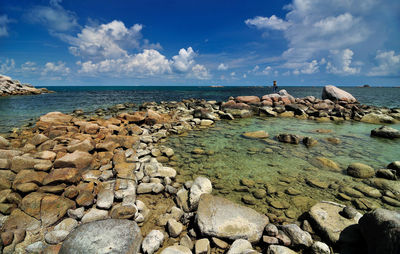 Rocks at shore against cloudy sky