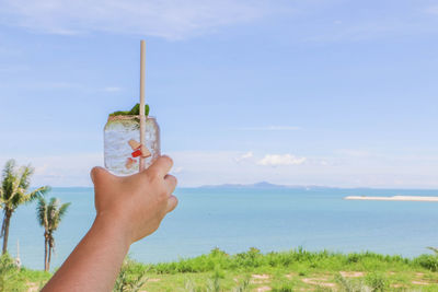 Midsection of person holding ice cream against sea