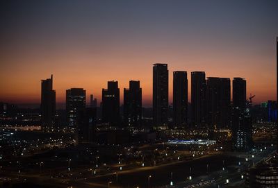 Illuminated buildings in city against sky at sunset