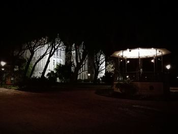 Illuminated road by building against sky at night