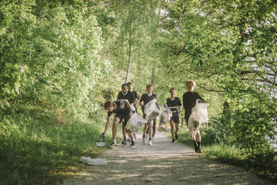 Boys plogging on footpath amidst green plants and trees