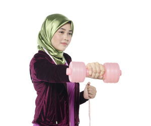 Young woman in hijab lifting dumbbell against white background