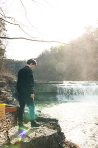 Side view of man standing by lake against trees