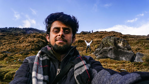 Portrait of young man standing on rock against sky