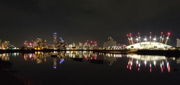 Illuminated buildings by river against sky at night