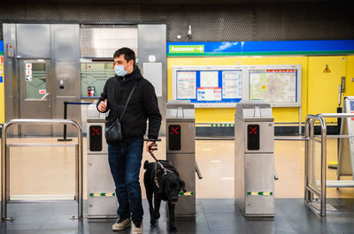 Full body of male in medical mask walking through automatic card reader with dog in metro