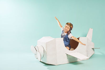 Portrait of smiling girl sitting in toy airplane over blue background