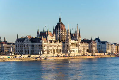 View of buildings by river against clear sky