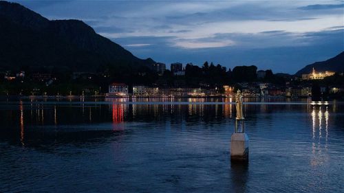 Scenic view of lake by illuminated city against sky at dusk