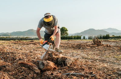 Mature unrecognizable man standing in field and starting modern chainsaw while getting ready for cutting tree trunk in rural area in highlands