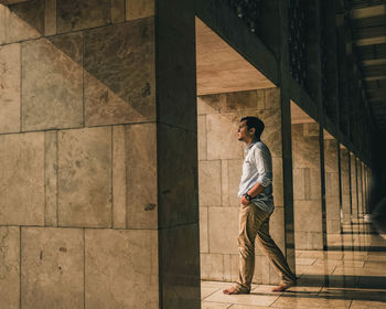 Side view of young man walking amidst architectural columns in corridor