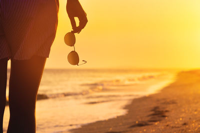 Low section of woman standing at beach during sunset
