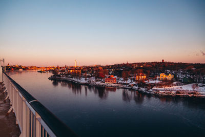 City by river against sky during sunset