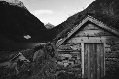 Old wooden house amidst mountains against sky