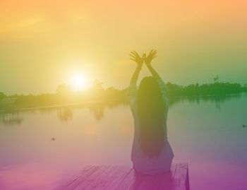 Rear view of woman standing by lake against sky during sunset