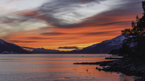 Scenic view of sea by snowcapped mountains against sky during sunset