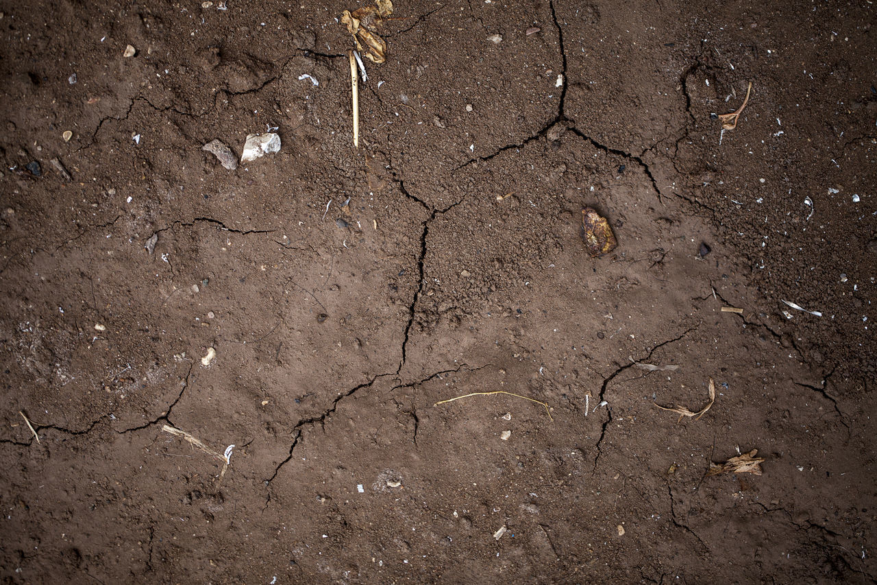 HIGH ANGLE VIEW OF CRACKED LAND ON DRY FIELD