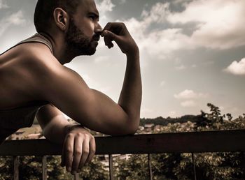 Man looking away by railing against sky