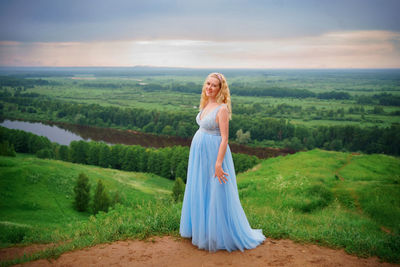 Pregnant woman in blue dress, green hills, river and sky