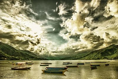 Boats in calm sea against cloudy sky