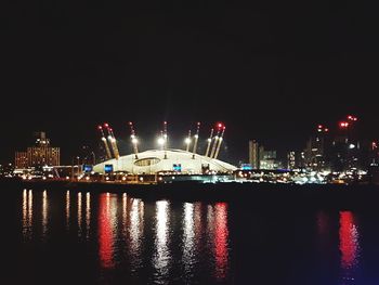 Illuminated buildings by river against sky at night