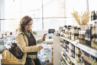 Woman holding smart phone while shopping in supermarket