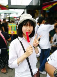 Portrait of woman showing peace sign while holding popsicle