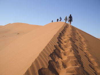 Rear view of people walking on sand dune against clear sky