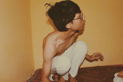 Side view of young man sitting against wall at home