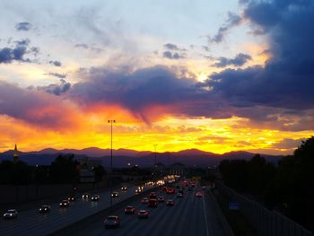 Vehicles on road against dramatic sky during sunset