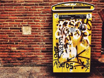 Graffiti on yellow garbage can against brick wall