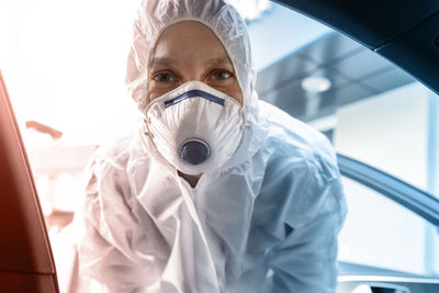 Portrait of doctor in protective wear looking in car