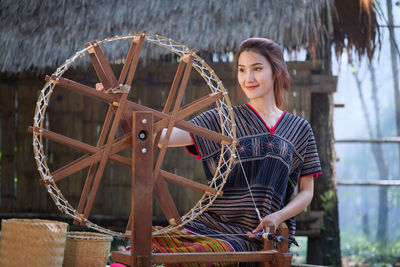 Young woman weaving thread on wheel against house