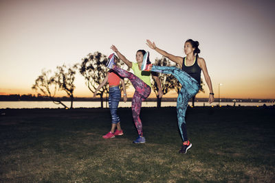 Sportswomen exercising on field against clear sky at park during sunset