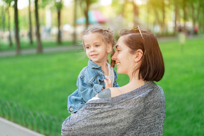 Smiling mother carrying cute daughter in park