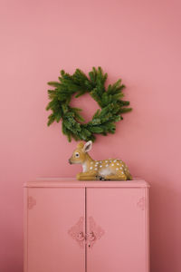 Souvenir fawn on a pink dresser against a pink wall on which hangs a christmas tree. copy space