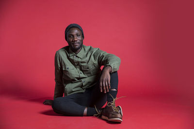 Portrait of young man sitting against red background