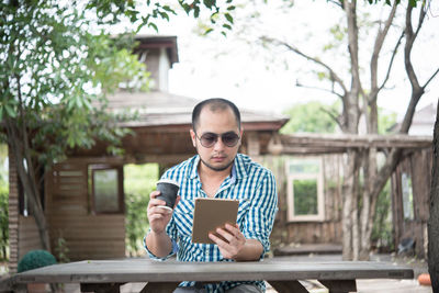 Man with disposable cup using digital tablet outdoors