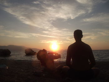 Father and daughter sitting at beach against sky