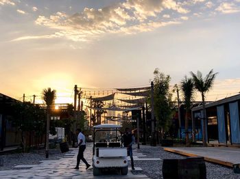 People walking on street amidst buildings in city at sunset