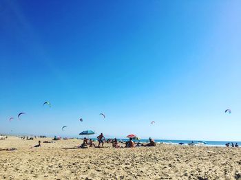 People at beach against clear blue sky