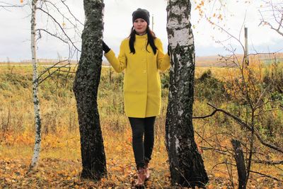 Portrait of young woman standing on tree trunk