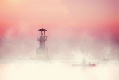 Lighthouse by sea against sky during sunset