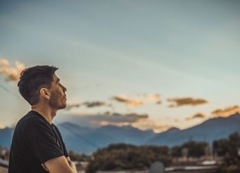 Side view of young man looking at mountain against sky