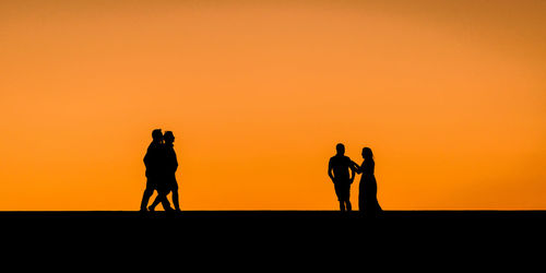 Silhouette friends standing against orange sky