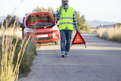A man talks on the phone while putting a warning triangle behind his vehicle.