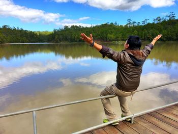 Rear view of man standing by lake against sky