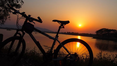 Silhouette bicycle by lake against sky during sunset