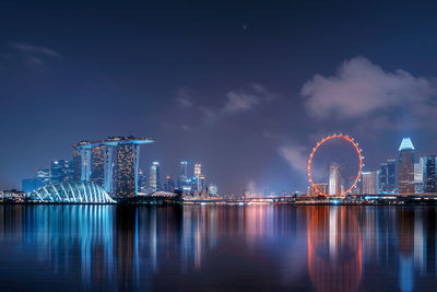 Illuminated modern buildings reflecting on river against sky in city at night