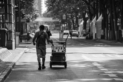 Rear view of man pushing cart on street in city